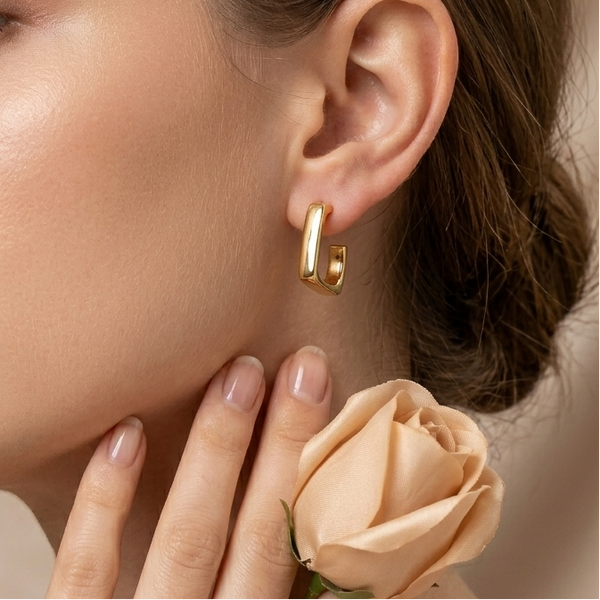 Close-up of a woman wearing gold hoop earrings with a soft focus on her face and hand holding a peach-colored rose.