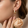 Close-up of a woman wearing gold hoop earrings with a soft focus on her face and hand holding a peach-colored rose.